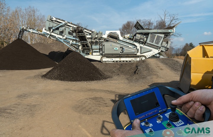 Granulator destruktu asfaltowego CAMS CENTAURO L 120.56 APR podczas pracy, na pierwszym planie pilot zdalnego sterowania z zamontowanym opcjonalnym wyświetlaczem typu LCD