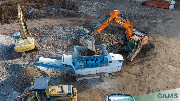 Granulator CAMS UTM 1500 podczas pracy w terenie, widać dwie koparki gąsienicowe, ładowarkę kołową i pryzmę usypaną z przetworzonego materiału przez granulator